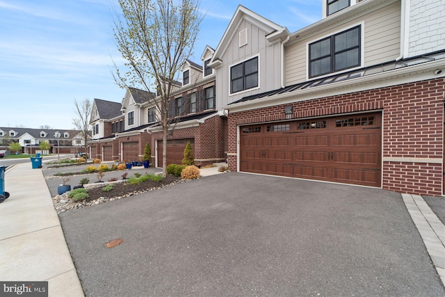 exterior space with aphalt driveway, board and batten siding, an attached garage, brick siding, and a residential view