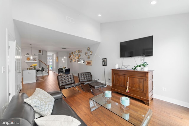 living area with visible vents, wood finished floors, baseboards, and stairway