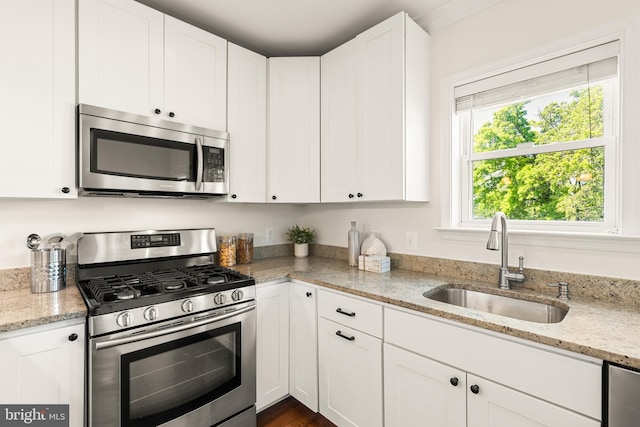 kitchen with light stone counters, a sink, white cabinets, and stainless steel appliances