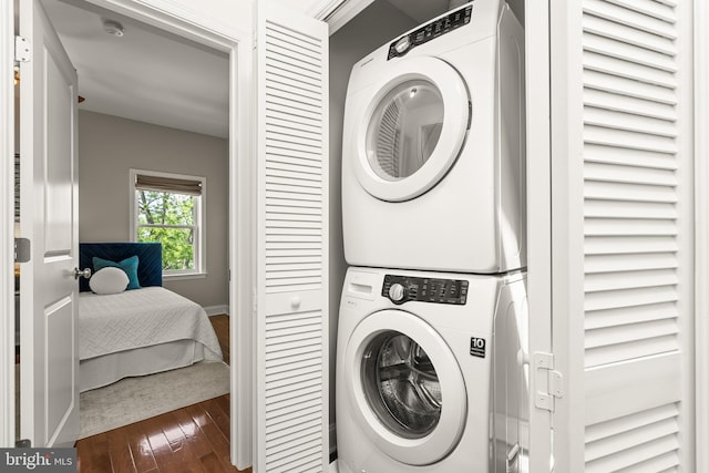 laundry area with laundry area, stacked washer and dryer, wood-type flooring, and baseboards
