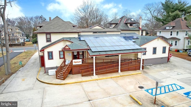 view of front of property featuring a porch, roof with shingles, a residential view, and solar panels