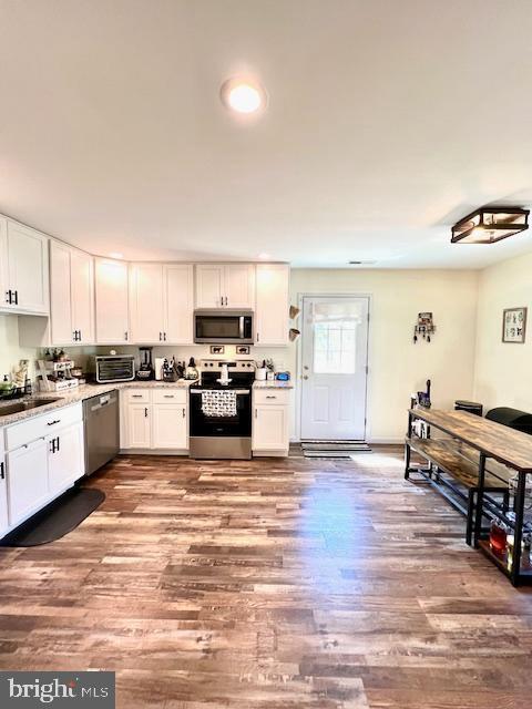 kitchen featuring stainless steel appliances, wood finished floors, white cabinets, a sink, and recessed lighting