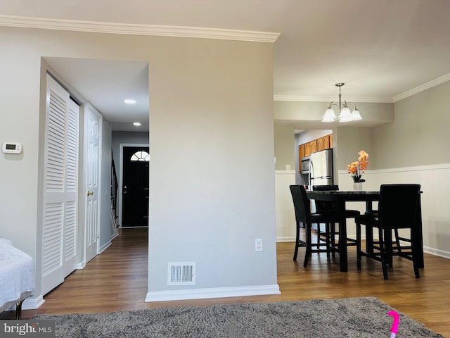 dining room featuring visible vents, wood finished floors, baseboards, a chandelier, and ornamental molding