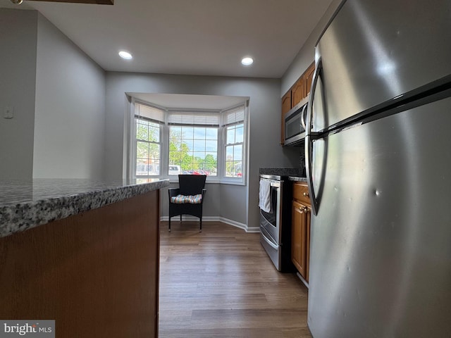 kitchen with brown cabinets, wood finished floors, baseboards, stainless steel appliances, and recessed lighting