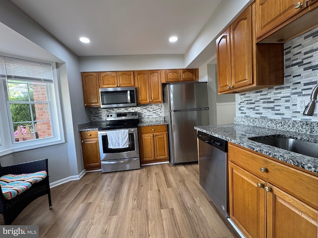 kitchen with light wood-style floors, decorative backsplash, dark stone counters, and stainless steel appliances