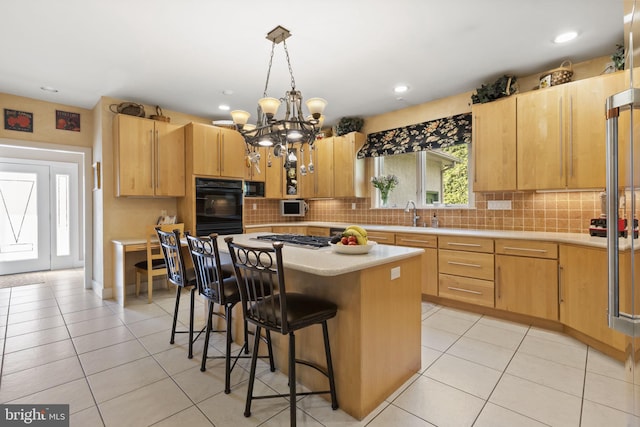 kitchen with an inviting chandelier, dobule oven black, light countertops, a kitchen breakfast bar, and gas cooktop