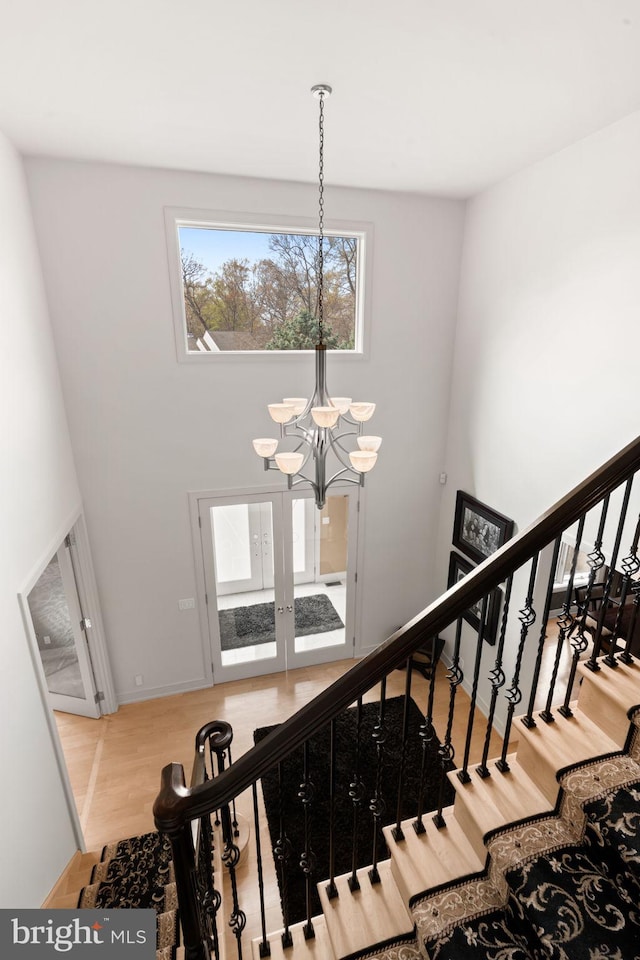 stairway featuring a chandelier, wood finished floors, a high ceiling, french doors, and baseboards