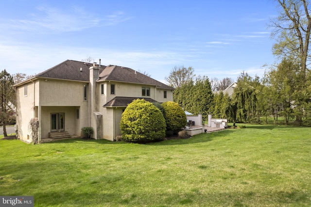 rear view of house featuring a yard, a chimney, and stucco siding