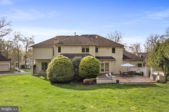 back of property with a patio area, roof with shingles, stucco siding, and a lawn