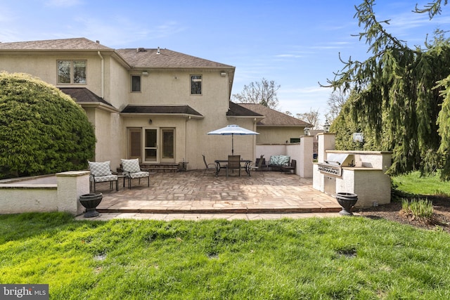 rear view of property with an outdoor kitchen, a patio area, stucco siding, and a yard