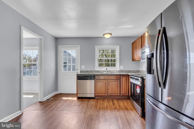 kitchen featuring brown cabinetry, wood finished floors, light stone counters, and appliances with stainless steel finishes