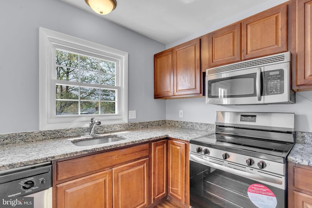 kitchen featuring brown cabinetry, appliances with stainless steel finishes, light stone countertops, and a sink