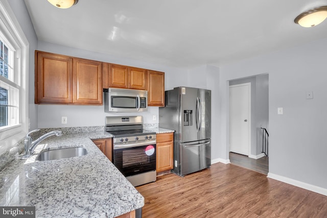 kitchen featuring stainless steel appliances, light stone counters, a sink, and plenty of natural light
