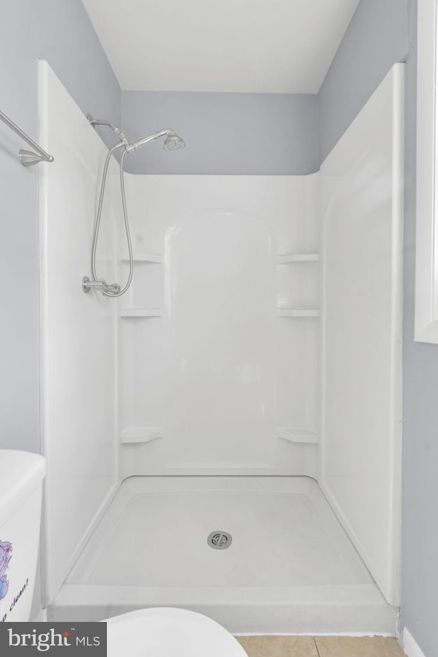 bathroom featuring toilet, tile patterned flooring, and a stall shower