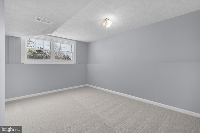 carpeted spare room featuring a textured ceiling, visible vents, and baseboards