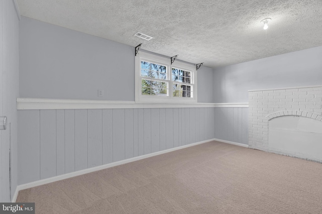 basement with carpet flooring, a textured ceiling, a wainscoted wall, and visible vents