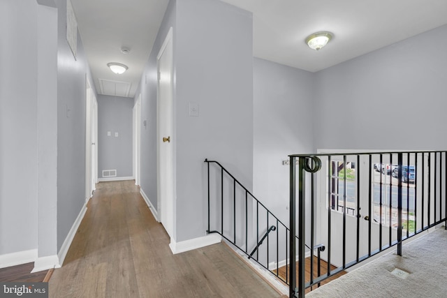 hallway featuring attic access, visible vents, baseboards, an upstairs landing, and wood finished floors
