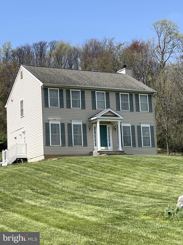 colonial home featuring a front lawn and a chimney