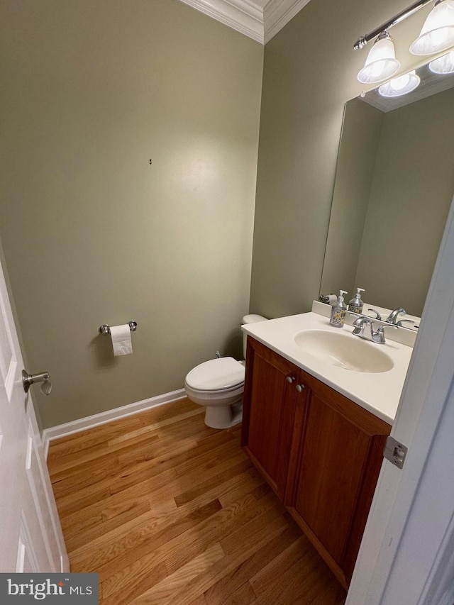 bathroom with baseboards, toilet, crown molding, vanity, and wood finished floors
