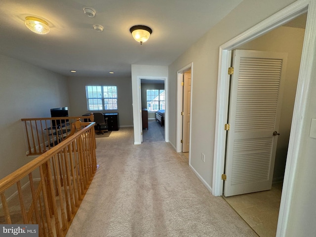 hall featuring light carpet, baseboards, and an upstairs landing