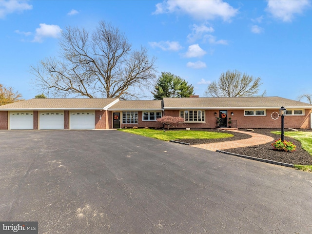 ranch-style home featuring an attached garage, aphalt driveway, and brick siding