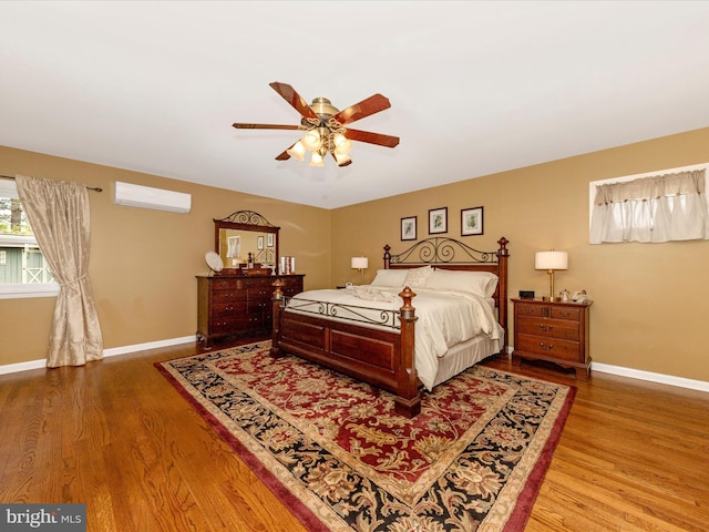 bedroom featuring baseboards, a ceiling fan, wood finished floors, and a wall mounted air conditioner