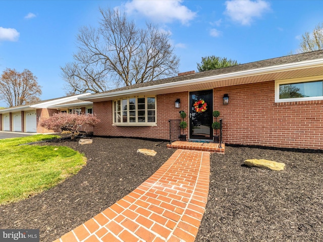view of front of home featuring an attached garage, a chimney, driveway, and brick siding