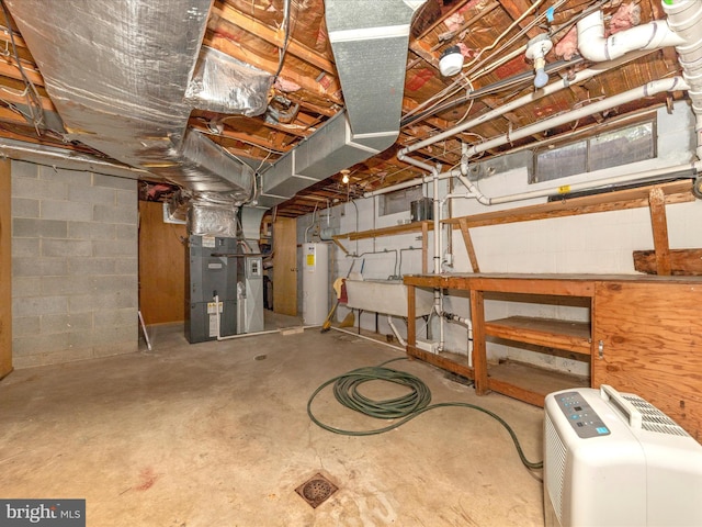 unfinished basement featuring water heater, concrete block wall, heating unit, and a sink