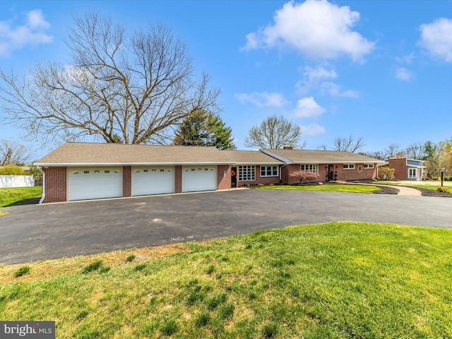 ranch-style home with aphalt driveway, a front yard, brick siding, a chimney, and a garage