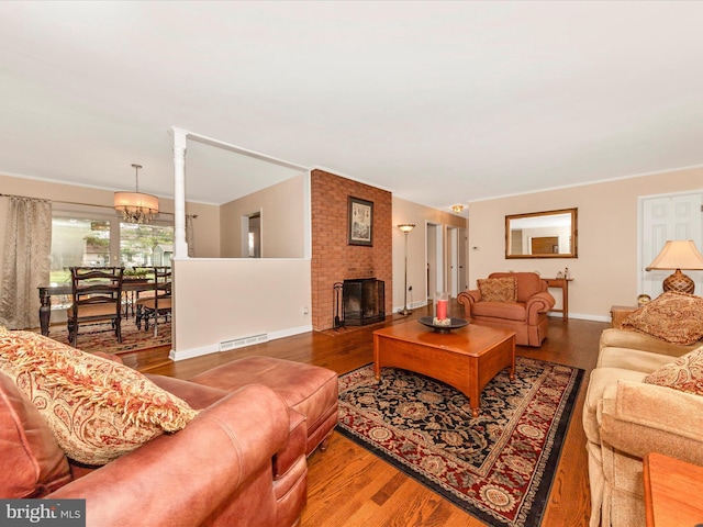 living room featuring ornamental molding, visible vents, a chandelier, wood finished floors, and a brick fireplace