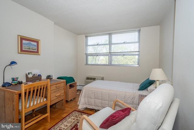bedroom featuring baseboard heating, a wall mounted air conditioner, and a textured ceiling