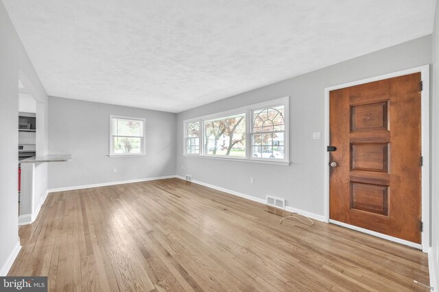 unfurnished living room with a textured ceiling, visible vents, wood finished floors, and baseboards