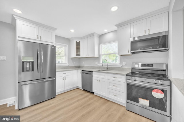 kitchen with white cabinets, stainless steel appliances, light wood-style flooring, and a sink