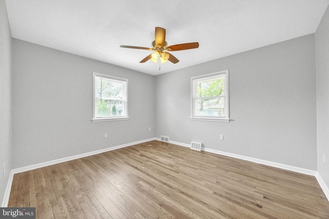 unfurnished room featuring wood finished floors, visible vents, plenty of natural light, and baseboards