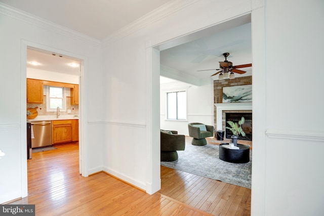 hallway featuring light wood-type flooring, a sink, crown molding, and baseboards