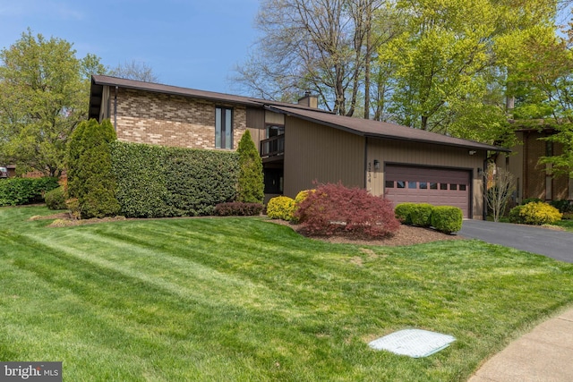 single story home with a front yard, an attached garage, a chimney, brick siding, and driveway