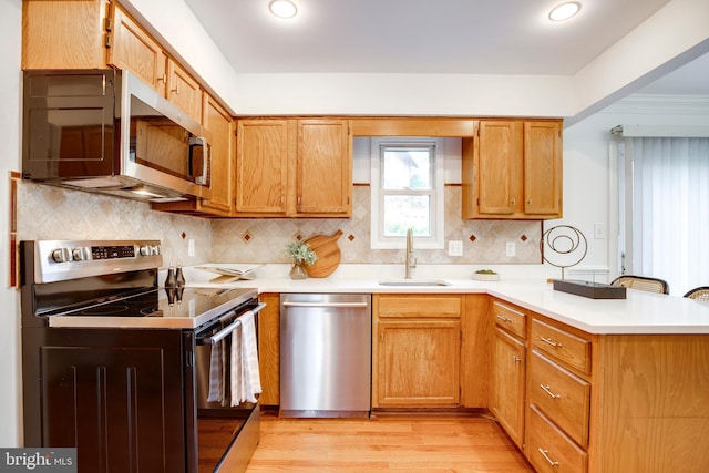 kitchen with a peninsula, light wood-type flooring, light countertops, a sink, and stainless steel appliances