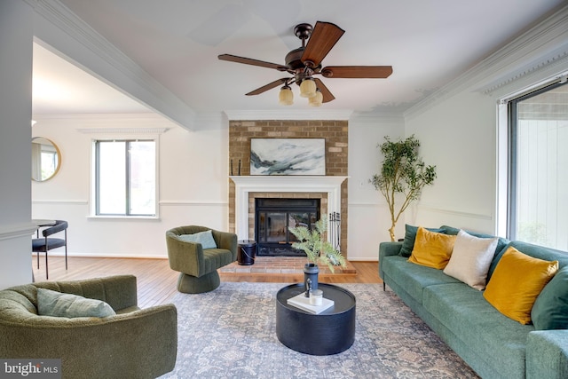 living area with baseboards, a fireplace, crown molding, a ceiling fan, and wood finished floors