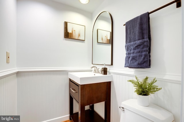 bathroom with a decorative wall, vanity, wainscoting, and toilet