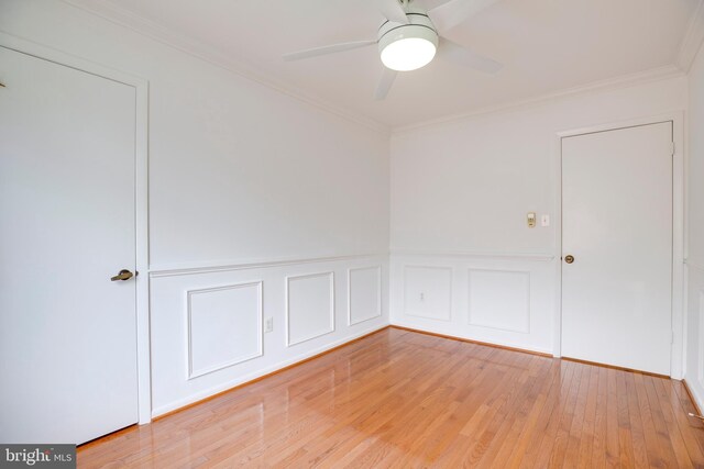 empty room with a decorative wall, ornamental molding, ceiling fan, a wainscoted wall, and light wood-style flooring