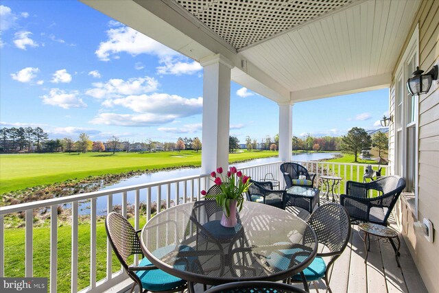 exterior space featuring view of golf course, a lawn, outdoor dining area, and a water view