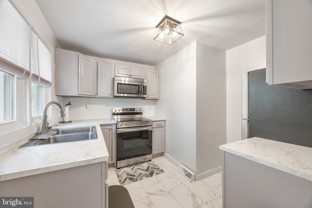 kitchen with a sink, decorative backsplash, marble finish floor, stainless steel appliances, and light stone countertops