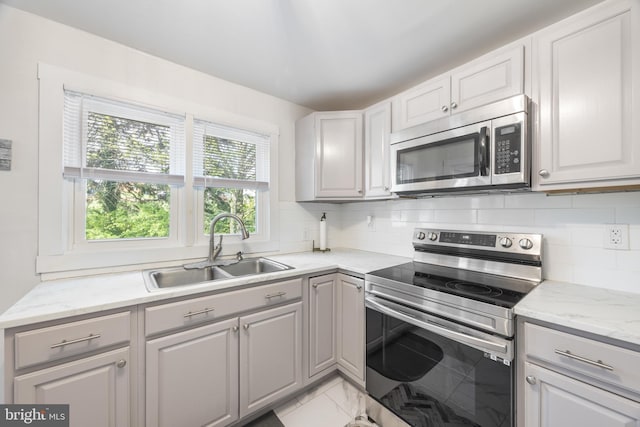 kitchen with stainless steel appliances, gray cabinetry, a sink, and tasteful backsplash