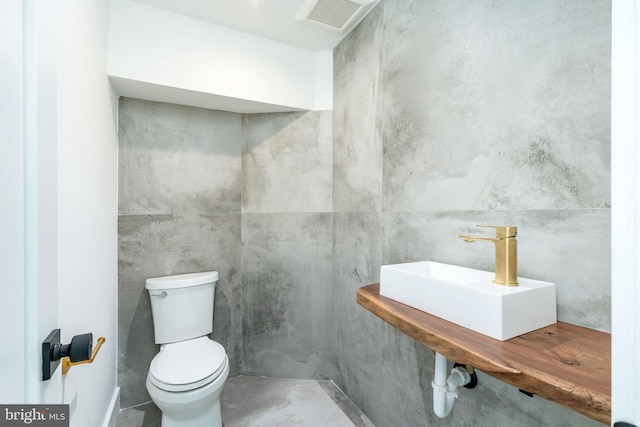 half bath featuring toilet, a sink, and concrete flooring