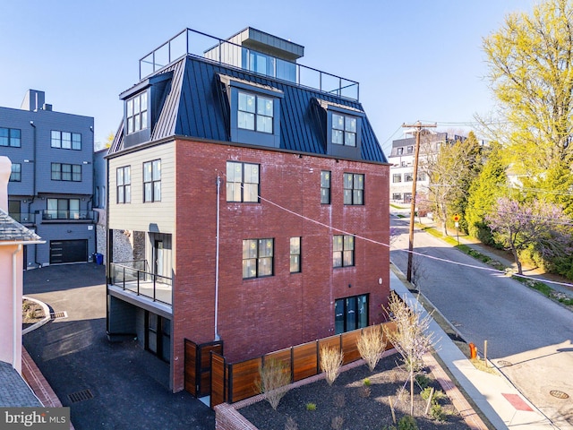 view of property exterior featuring metal roof, a standing seam roof, brick siding, a balcony, and fence