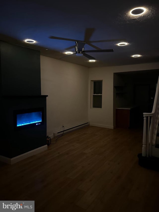 unfurnished living room featuring a glass covered fireplace, a baseboard heating unit, baseboards, recessed lighting, and wood finished floors