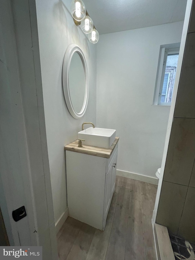 half bath with wood finished floors, vanity, and baseboards