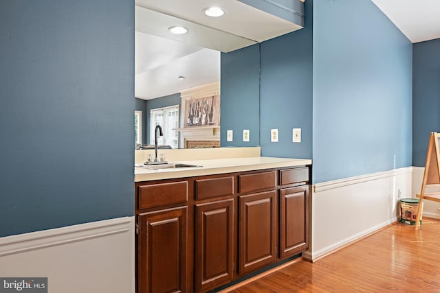 kitchen with light countertops, light wood-style flooring, a wainscoted wall, and a sink