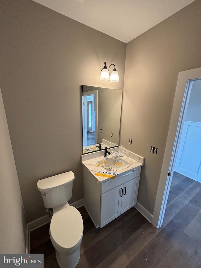 bathroom featuring toilet, vanity, wood finished floors, and baseboards