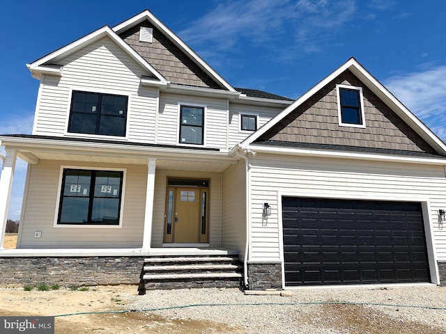 craftsman inspired home with an attached garage, concrete driveway, covered porch, and stone siding